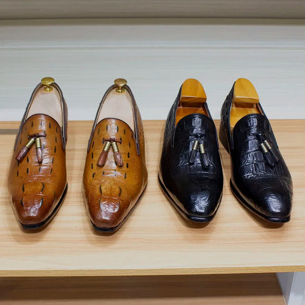 Two pairs of brown and black leather shoes with tassels on a wooden surface.