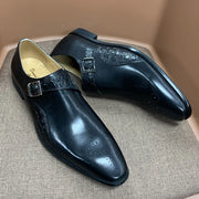Pair of black dress shoes with buckle details on a textured surface