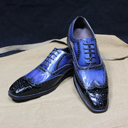 Blue and black shiny dress shoes on a beige surface with a dark background
