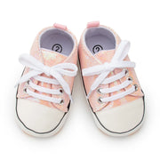 Pair of pink glittery baby shoes with white laces on a white background