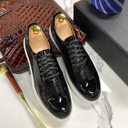 Black shiny shoes with gold accents on a marble surface with a brown textured bag and blue tie.