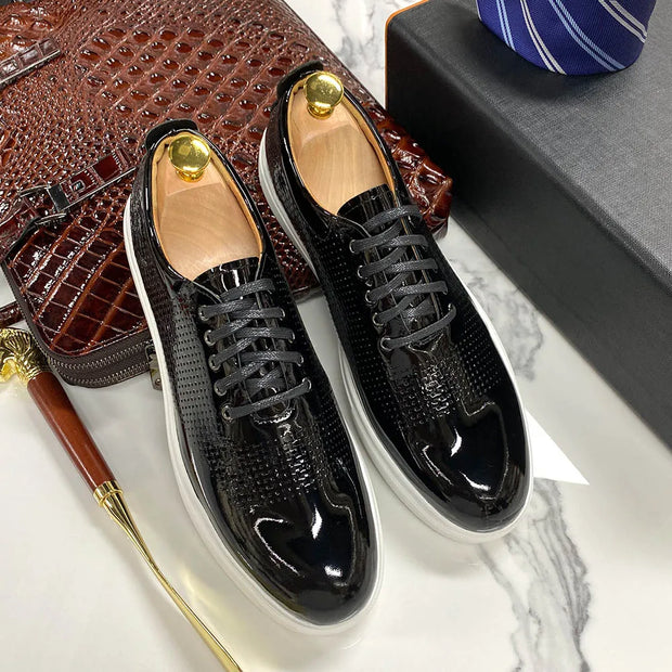 Black shiny shoes with gold accents on a marble surface with a brown textured bag and blue tie.