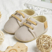 Beige baby shoes with yellow laces on a white surface with decorative elements.
