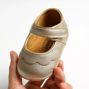Gold baby shoe held by a hand on a white background