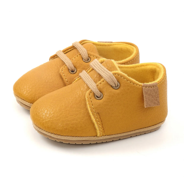 Pair of mustard yellow baby shoes with brown laces on a white background