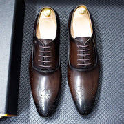 Pair of brown dress shoes with gold accents on a textured gray surface