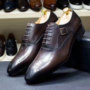 Pair of brown leather dress shoes with a buckle on a textured surface.