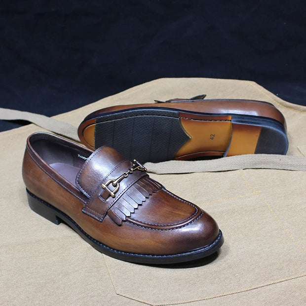 Brown leather loafers on a beige surface with a dark background