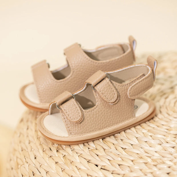 Pair of beige baby sandals on a woven surface