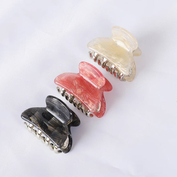 Three butterfly-shaped hair clips in black, pink, and beige on a white background