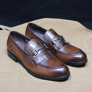 Pair of brown leather loafers with decorative metal accents on a beige surface.