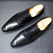 Pair of black dress shoes with gold soles on a textured gray surface