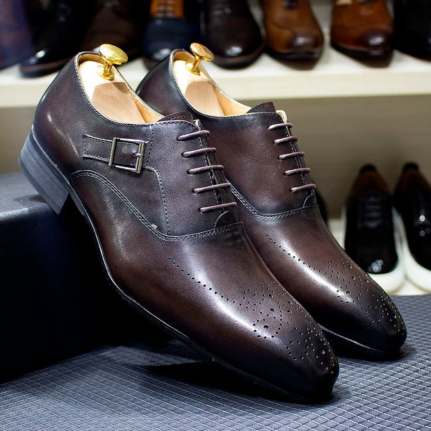 Pair of brown leather dress shoes with a buckle on a textured surface.