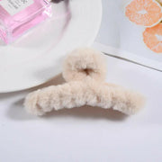 Fluffy beige hair clip on a white surface with a bottle of perfume and orange slices in the background.