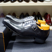 Black leather dress shoes with a wooden shoe tree on a textured surface.