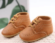 Pair of brown baby shoes on a textured surface with a blurred green leaf background.