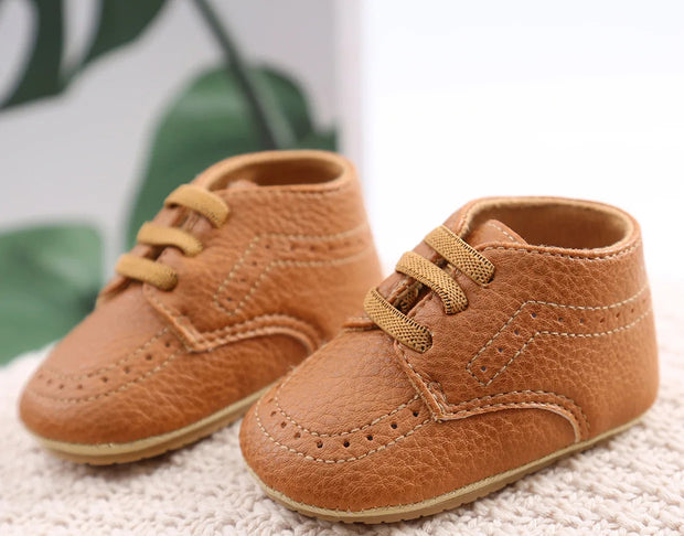 Pair of brown baby shoes on a textured surface with a blurred green leaf background.