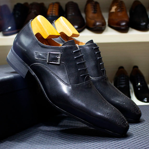 Black dress shoes with yellow soles on a textured surface, with more shoes in the background.