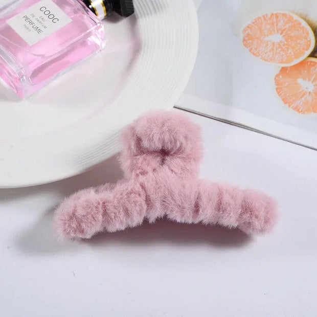 Pink fuzzy hanger on a white surface with a bottle of perfume and a bag in the background.