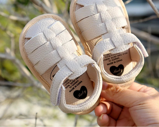 Baby sandals with woven design held by a hand against a natural background