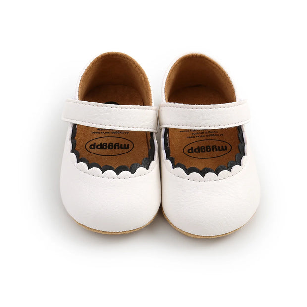 Pair of white baby shoes with brown soles on a white background
