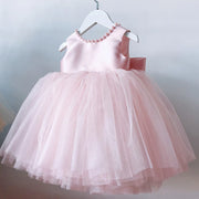 Pink children's dress with a bow on a hanger against a light background