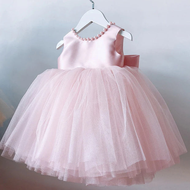 Pink children's dress with a bow on a hanger against a light background