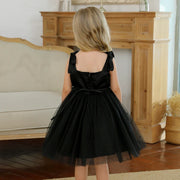 Young girl wearing a black dress with a bow detail in a room with wooden furniture.