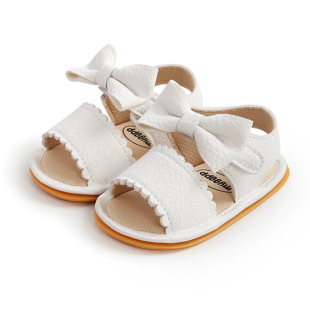 Pair of baby sandals with white lace details and brown soles on a white background