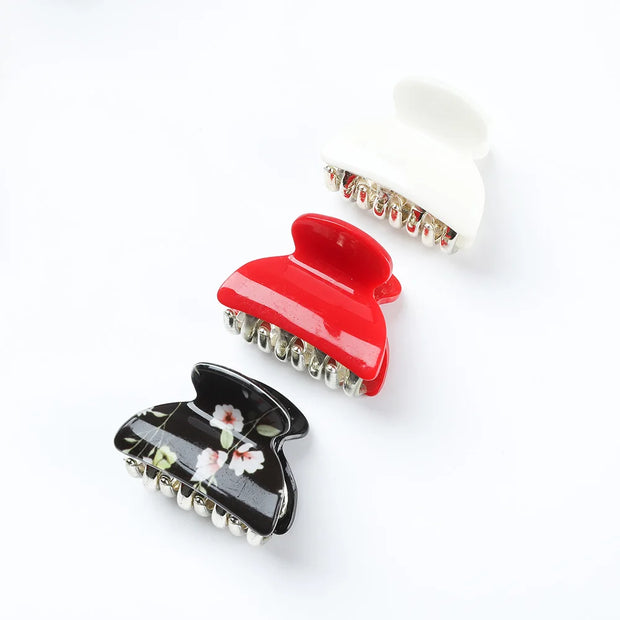Three hair clips in red, black with floral design, and white on a white background