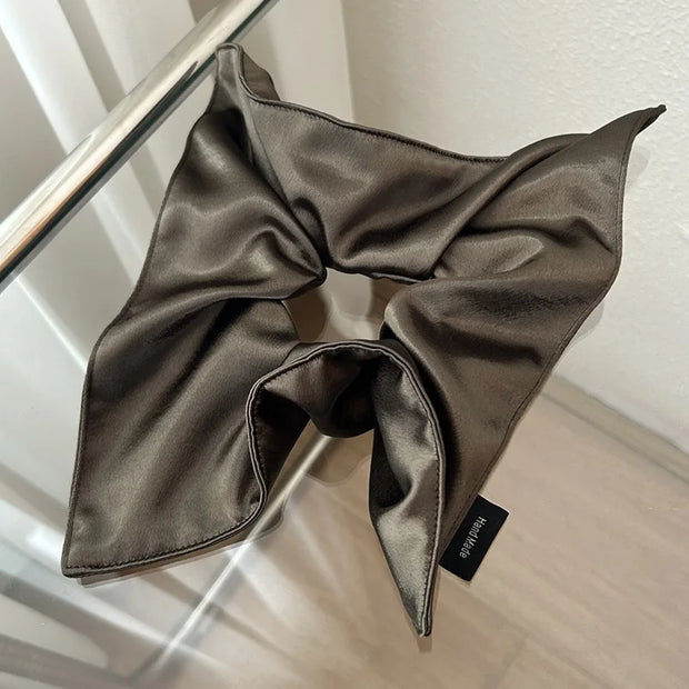 Brown satin hair scarf with a brand label on a reflective surface