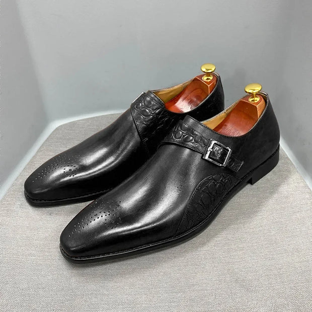 Pair of black leather dress shoes with gold buckles on a gray surface.