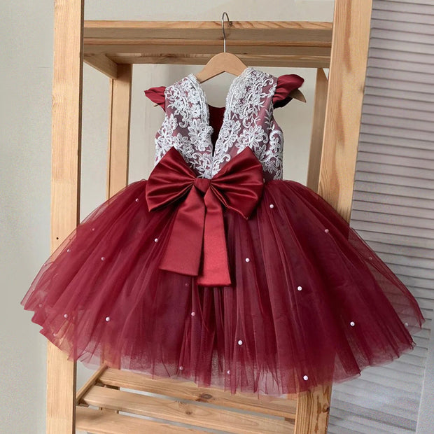 Red dress with lace top and large bow on a wooden hanger against a neutral background