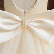 Close-up of a cream-colored dress with a large bow and pearl embellishments on a mannequin.