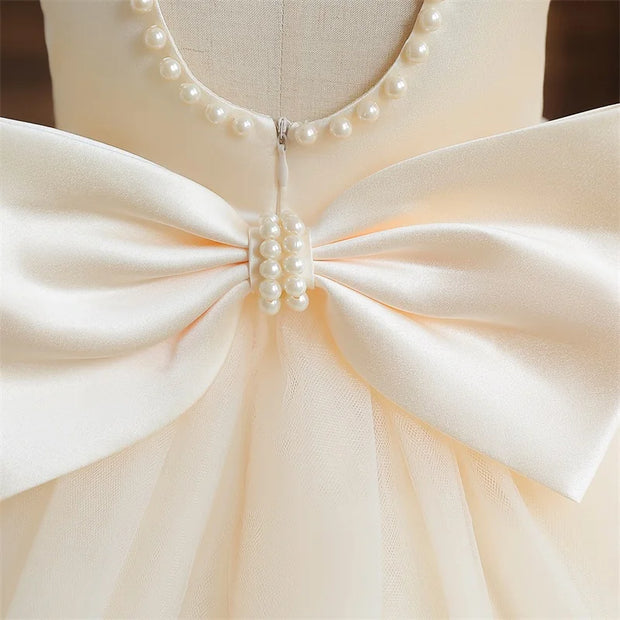 Close-up of a cream-colored dress with a large bow and pearl embellishments on a mannequin.