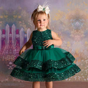 Young girl wearing a green sequin dress with a decorative headband against a colorful, abstract background.