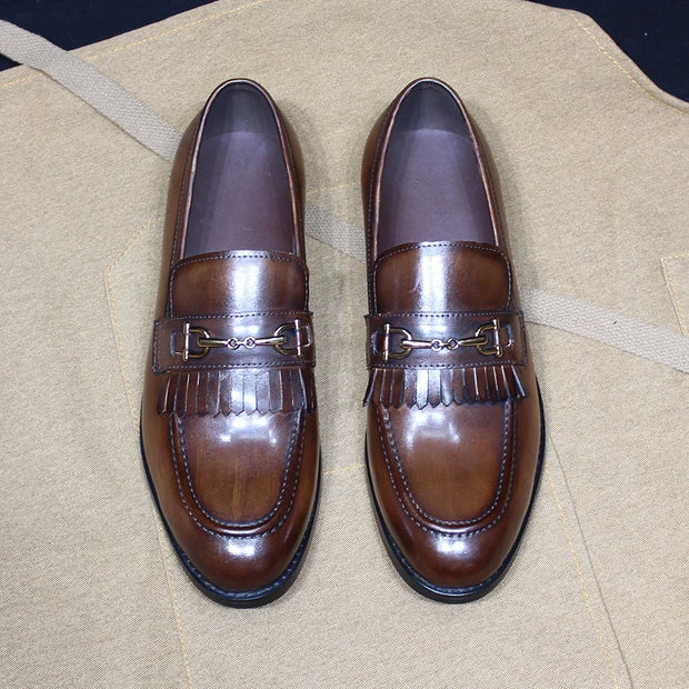 Pair of brown loafers with decorative buckle on a beige surface