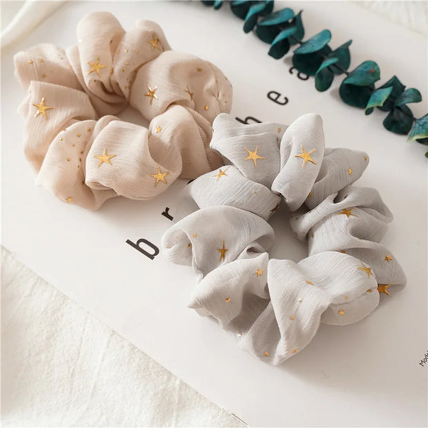 Beige and gray scrunchies with star patterns on a white surface.