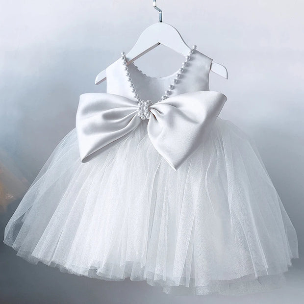 White children's dress with a large bow on a hanger against a light gray background