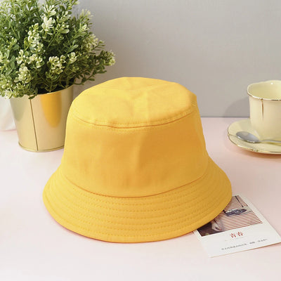 Yellow bucket hat on a table with a plant and cup in the background