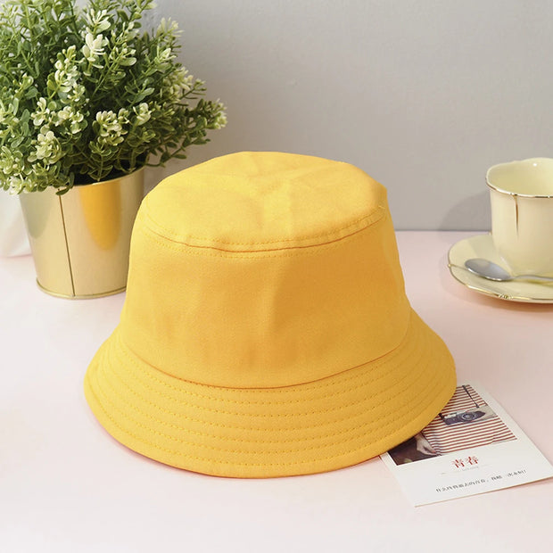 Yellow bucket hat on a table with a plant and cup in the background
