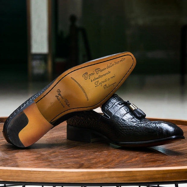 Black leather dress shoes with a brown sole on a wooden surface