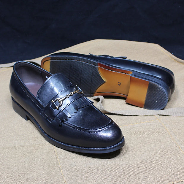 Navy blue loafers with a gold buckle on a beige surface