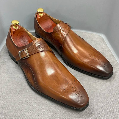 Pair of brown leather dress shoes with gold buckles on a light gray background