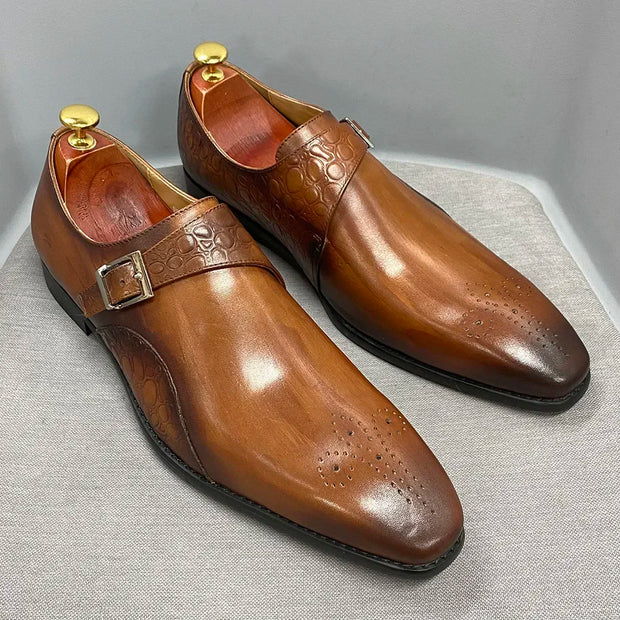 Pair of brown leather dress shoes with gold buckles on a light gray background