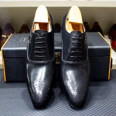 Pair of black dress shoes with gold accents on a textured surface.