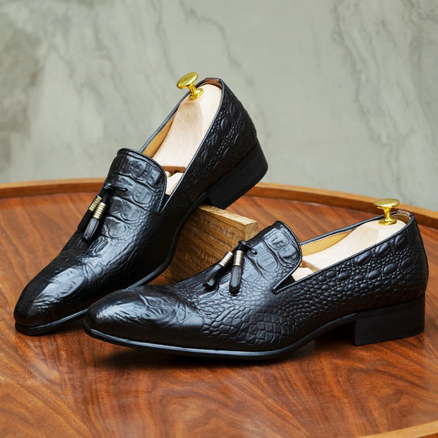 Black textured dress shoes on a wooden surface with a neutral background
