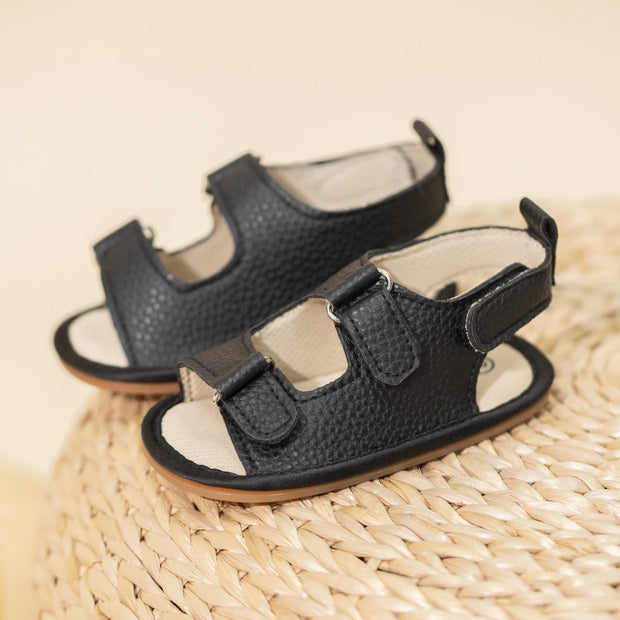 Pair of black baby sandals on a woven mat