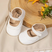 White baby shoes with a straw hat and flowers on a beige surface