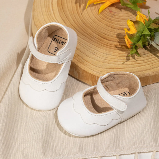White baby shoes with a straw hat and flowers on a beige surface